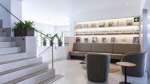 A modern interior with a staircase, seating area, and a wall displaying books and framed pictures. - Hotel Kivir Sevilla (Seville)