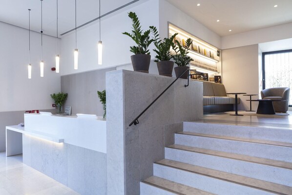 A reception area with a counter, potted plants, a staircase, and a seating area with a sofa and coffee table. - Hotel Kivir Sevilla (Seville)
