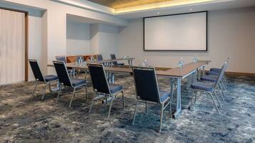A conference room with a large screen, multiple tables, and chairs.