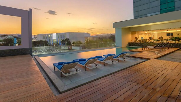 A rooftop pool area with lounge chairs and a view of the cityscape at sunset.