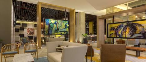 A modern lobby with seating areas, a large TV screen, and artwork on the walls.