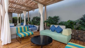 An outdoor seating area with a wooden floor, cushioned sofas, and a round table.