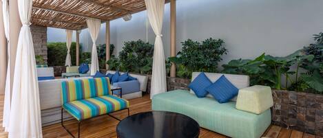 An outdoor seating area with a wooden floor, cushioned sofas, and a round table.