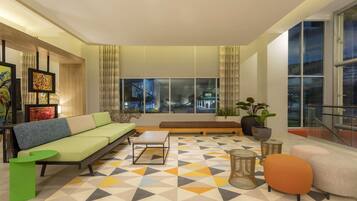 A modern living room with a sofa, coffee table, and seating area, large windows with city views, and a geometric patterned rug.