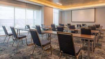 A conference room with long tables, chairs, a projector screen, and large windows.