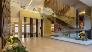 A spacious lobby with a modern staircase, a glass railing, and a seating area with tables and chairs.