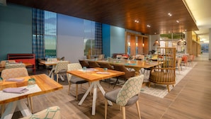 A modern dining area with wooden tables and chairs, a wooden ceiling, and large windows.