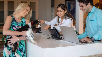 A reception desk with a laptop, a dog, and three people interacting.