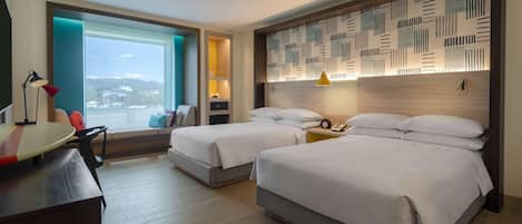 A hotel room with two beds, a desk, a chair, a window with a view, and a patterned headboard.