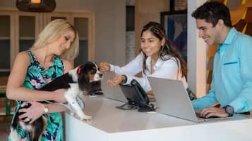 A reception desk with a laptop, a dog, and three people interacting.
