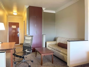 A hotel room with a desk, office chair, sofa, and a wardrobe.