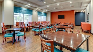 A dining area with multiple tables and chairs, a flat-screen TV mounted on the wall, and large windows allowing natural light. - Drury Inn Suites Phoenix Chandler Fashion Center (Phoenix)