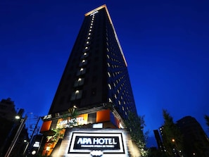 A tall building with a sign for APA HOTEL at the base, featuring a modern design with illuminated windows.