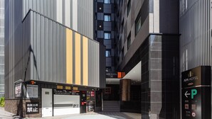 Entrada de hotel moderna com balcão de check-in, placa de estacionamento e escadas que levam aos andares superiores.