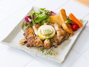 Un plato cuadrado con pollo a la parrilla, verduras y un gajo de limón.