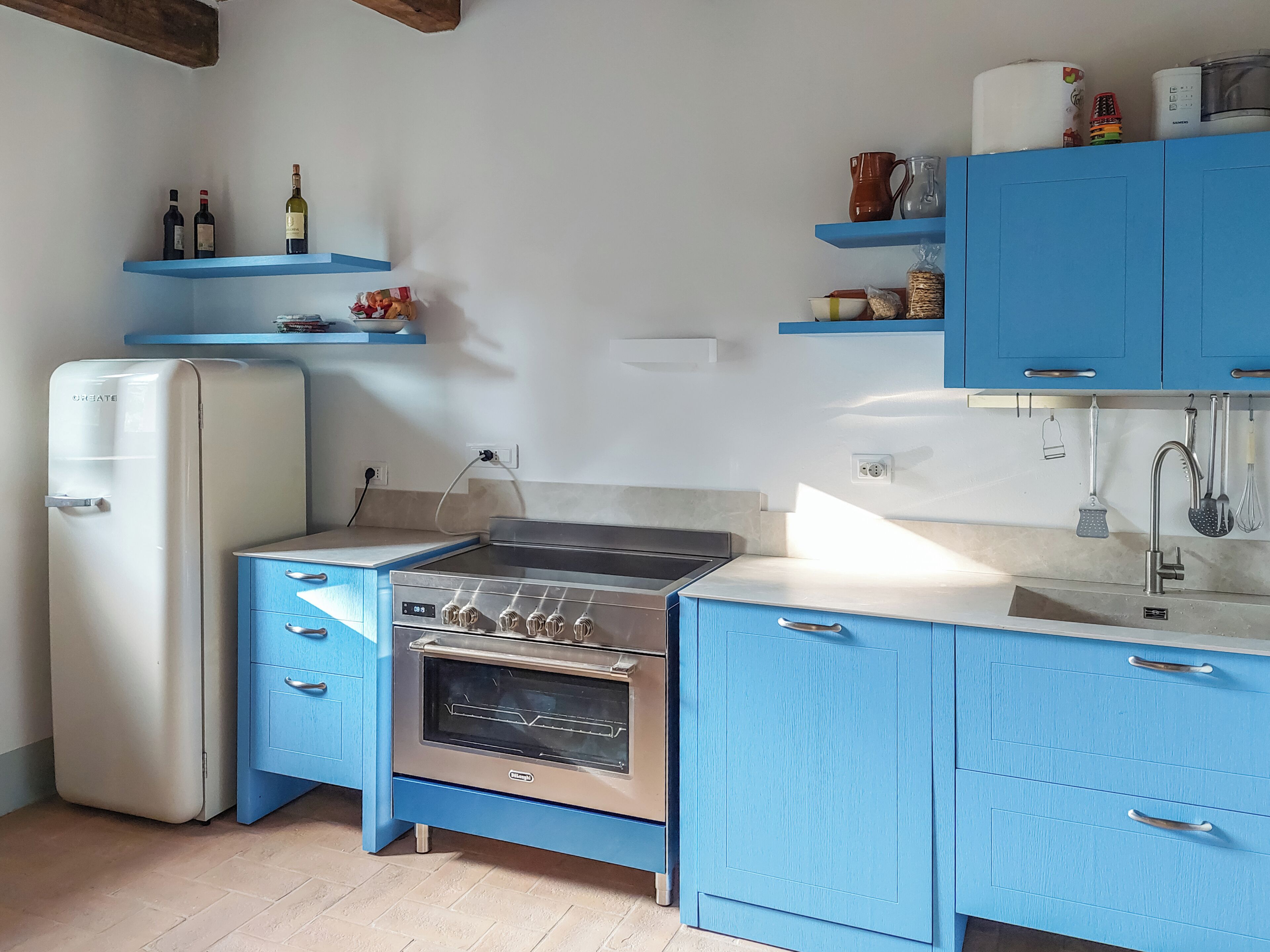 Een keuken met een koelkast, fornuis en blauwe kastjes.
