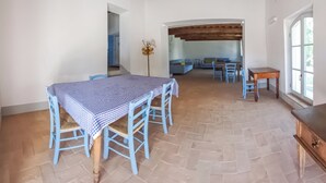 Een eetruimte met een geruit tafelkleed, blauwe stoelen, een houten bank en uitzicht op een woonkamer door een boog.