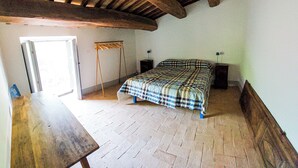 Een slaapkamer met een houten plafond, een bed met een geruite sprei, een houten tafel en een raam.