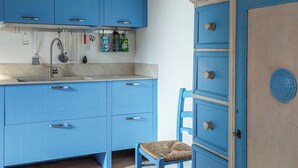 Een keuken met blauwe kastjes, een spoelbak en een stoel.