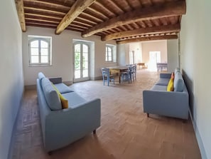 A spacious room with a wooden ceiling, two sofas, a dining table with chairs, and large windows. - Dimora Il Gello - Nel cuore della Val D'Orcia (Radicofani)