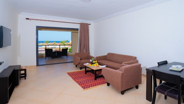 A living room with a sofa, a coffee table with fruit, a TV, and a dining table. - New Eagles Resort & Aqua Park (Hurghada)