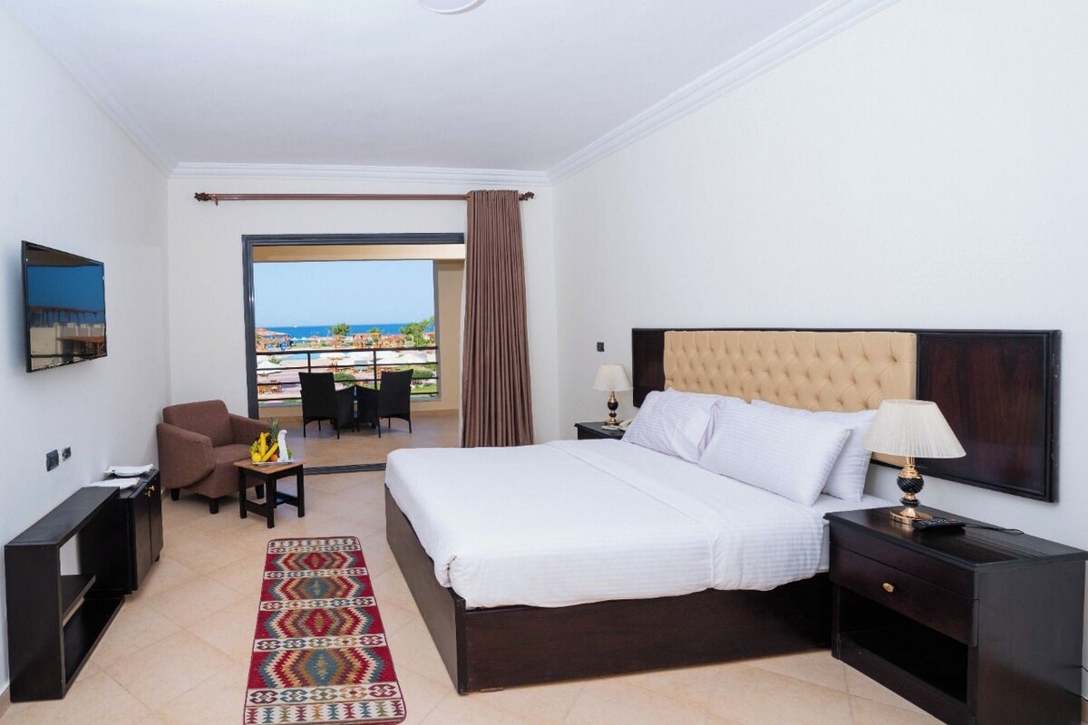 Ein Hotelzimmer mit Bett, Fernseher, Schreibtisch, Stuhl und Meerblick.