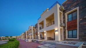 A modern hotel with multiple floors, outdoor seating areas, and a well-lit entrance. - New Eagles Resort & Aqua Park (Hurghada)
