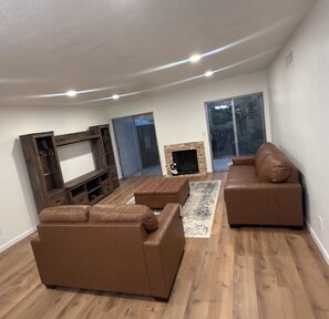 Ein Wohnzimmer mit Kamin, einer Couch, einem Fernseher und einem großen Fenster.