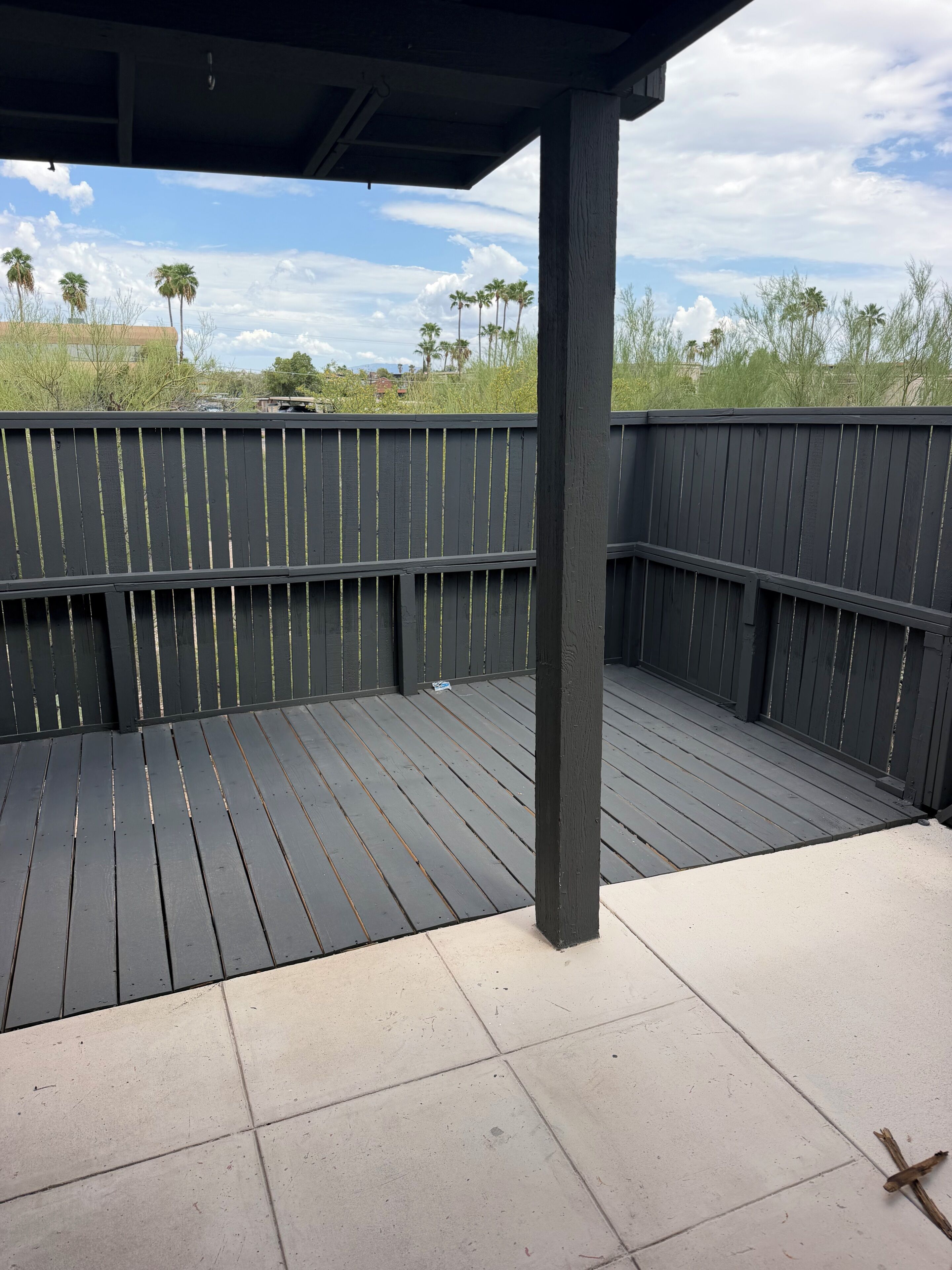 Een overdekt terras met houten vloer en uitzicht op palmbomen en een heldere lucht.