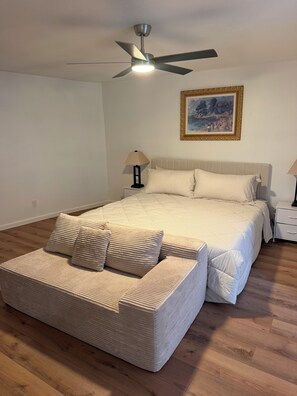 Ein Schlafzimmer mit einem Bett, einem Nachttisch, einer Lampe, einem Deckenventilator und einem Gemälde an der Wand.
