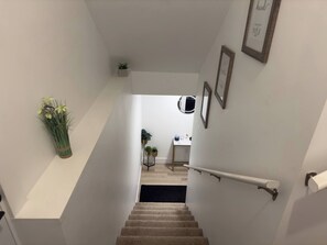 A staircase leading to a room with a small table, potted plants, and framed pictures on the walls. - Private 1BR Basement Suite Near YQM With Free Parking (Dieppe)