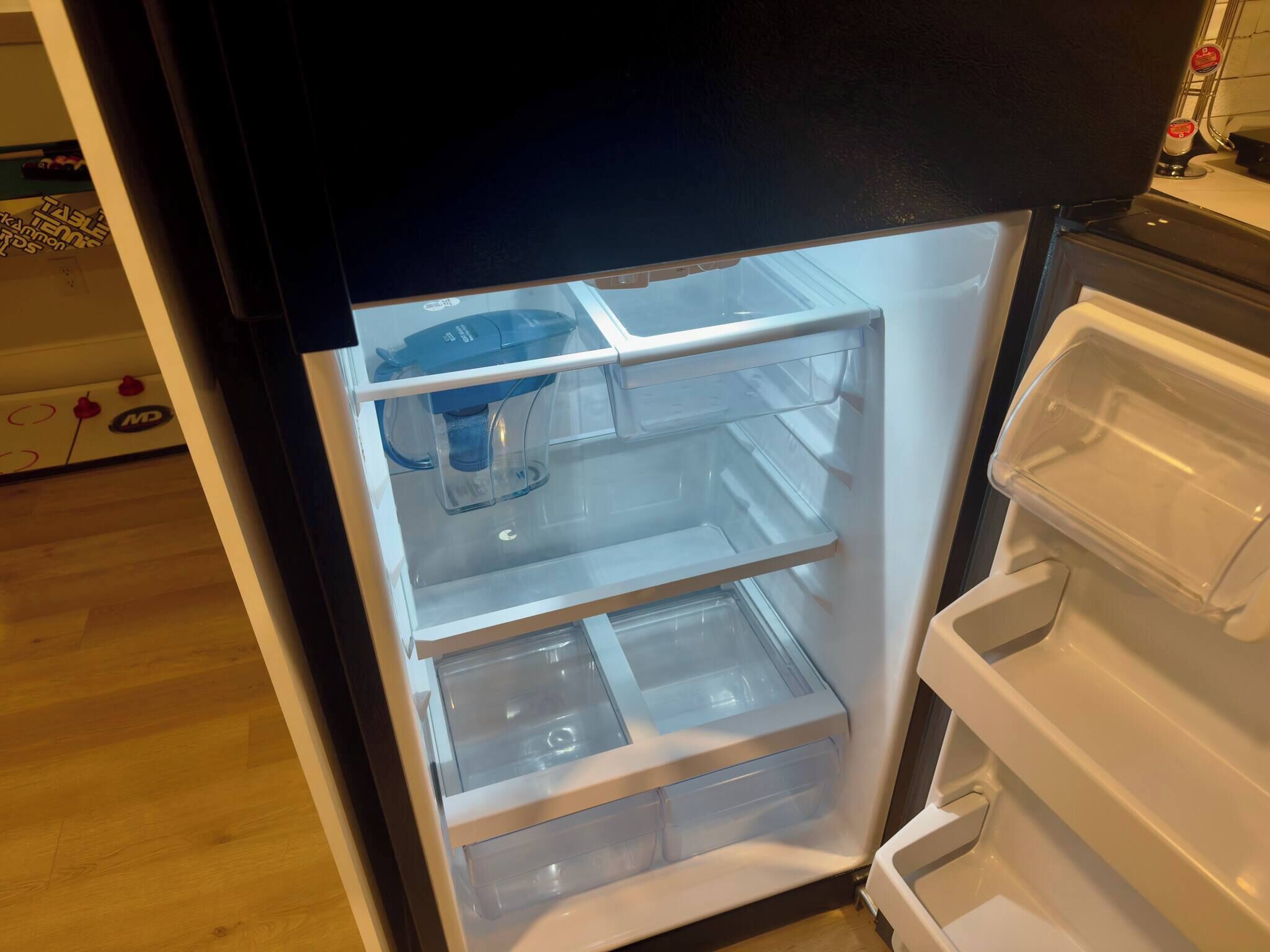 An open refrigerator with clear shelves and a water dispenser.