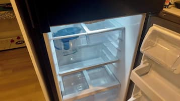 An open refrigerator with clear shelves and a water dispenser.
