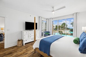 Ein Hotelzimmer mit Bett, Fernseher, Schreibtisch und Blick auf Pool und Palmen.