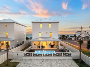 Uma casa branca de dois andares com piscina, área de estar externa e vista para o oceano.