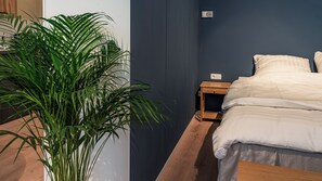 Ein Schlafzimmer mit einem Bett, einem Nachttisch, Holzboden und einer Topfpflanze.
