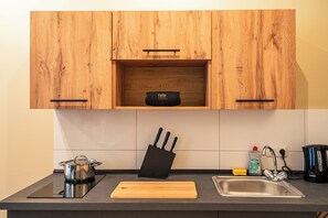 Eine Küche mit Holzausstattung, einem Messerblock, einem Schneidebrett, einer Spüle, einem Wasserkocher und einem Topf auf einem Induktionskochfeld.