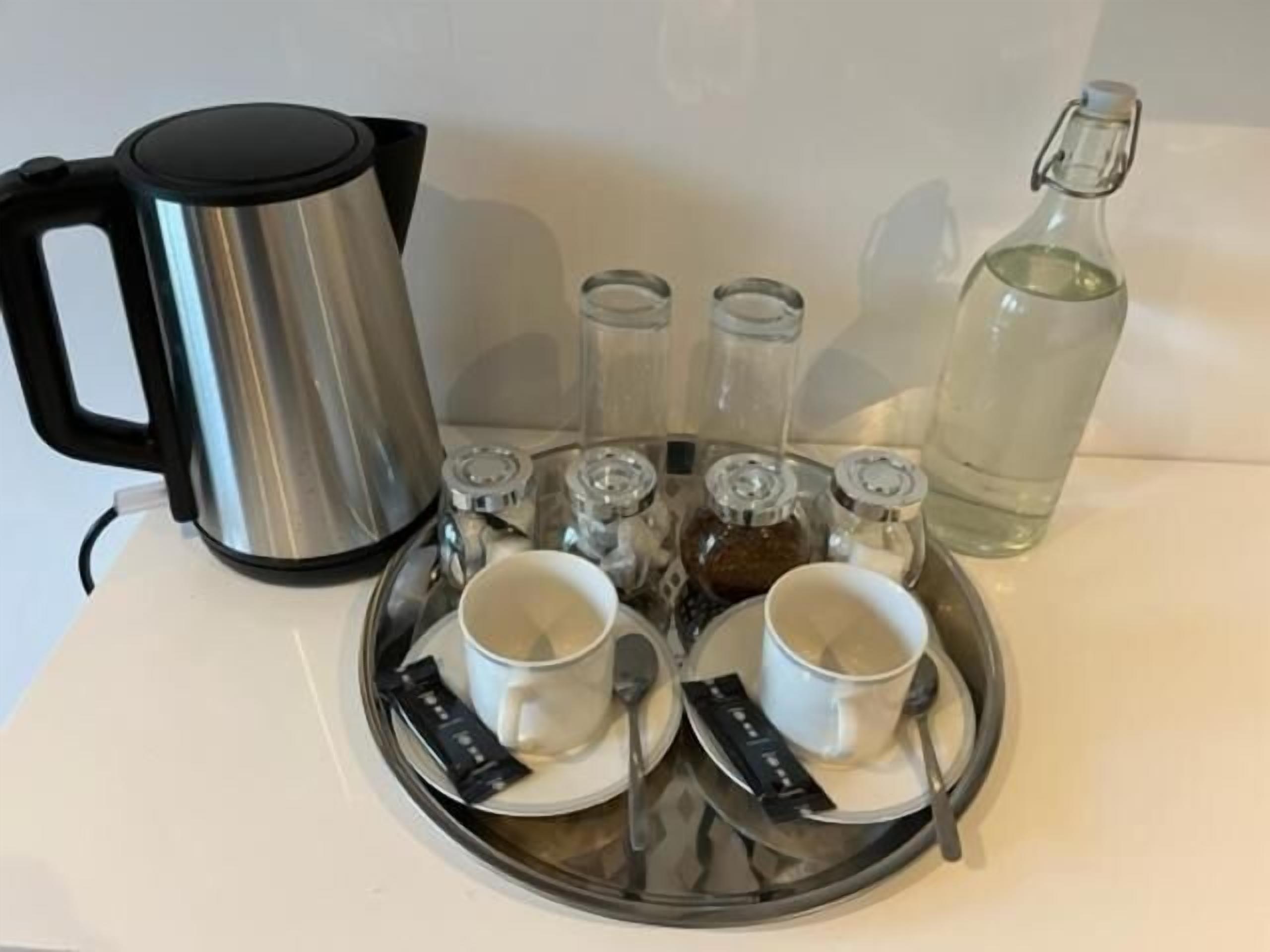 A tray with two white cups, a black coffee pot, and several glass containers with lids.