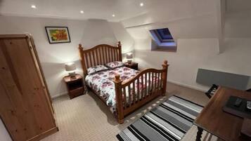 Une chambre à coucher avec un lit en bois, une table de chevet, un bureau, une chaise, une armoire, une fenêtre et un luminaire au plafond.