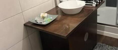 Un baño con tocador de madera, un lavabo blanco, un espejo y una zona de ducha.