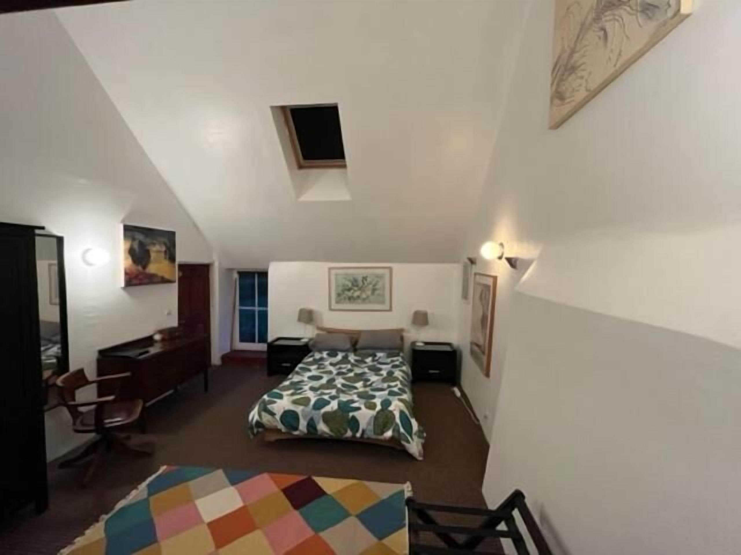 A bedroom with a bed, desk, chair, and a small window.