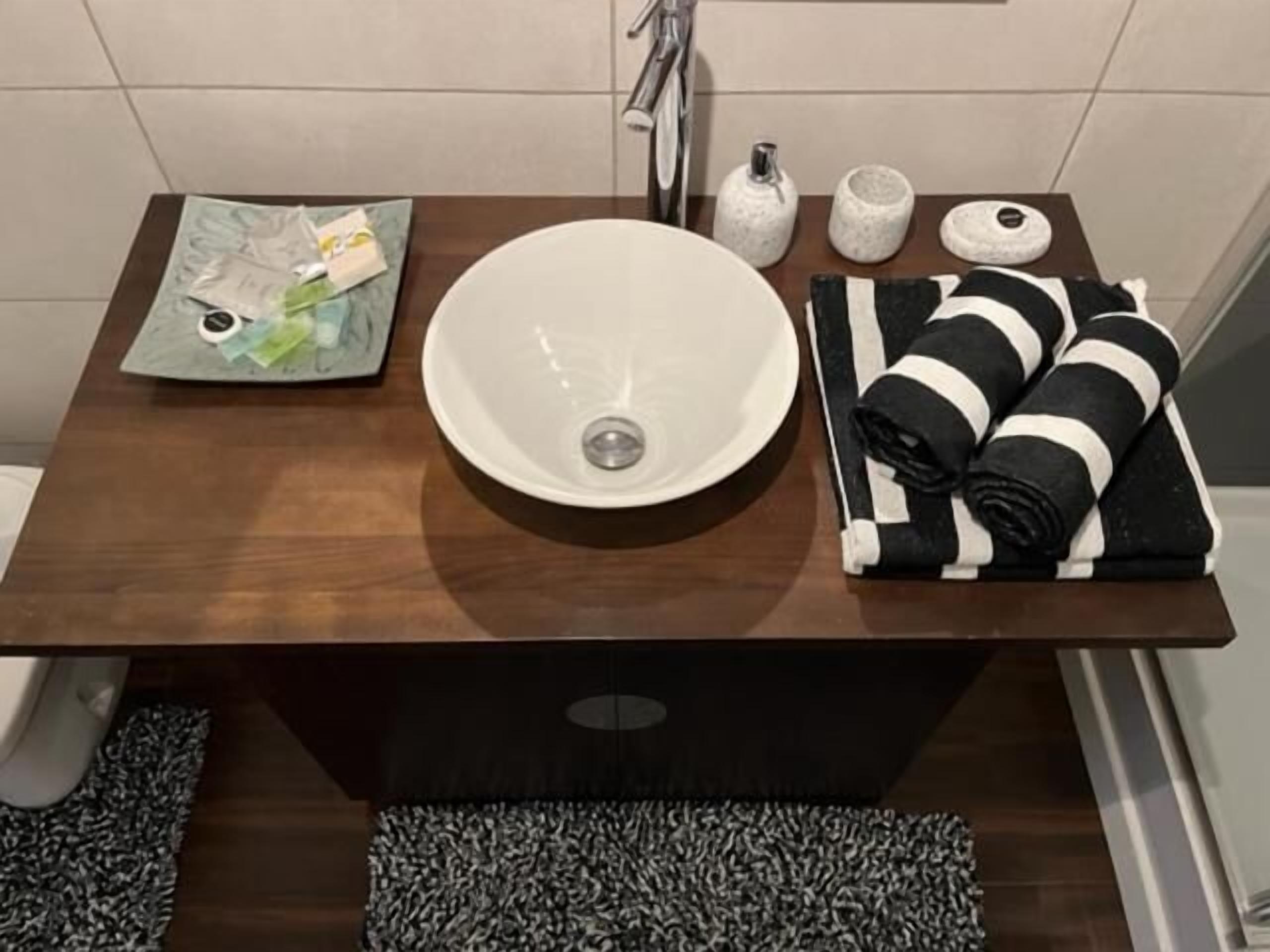A bathroom with a wooden vanity, a white sink, a towel rack with striped towels, and a small shelf with toiletries.