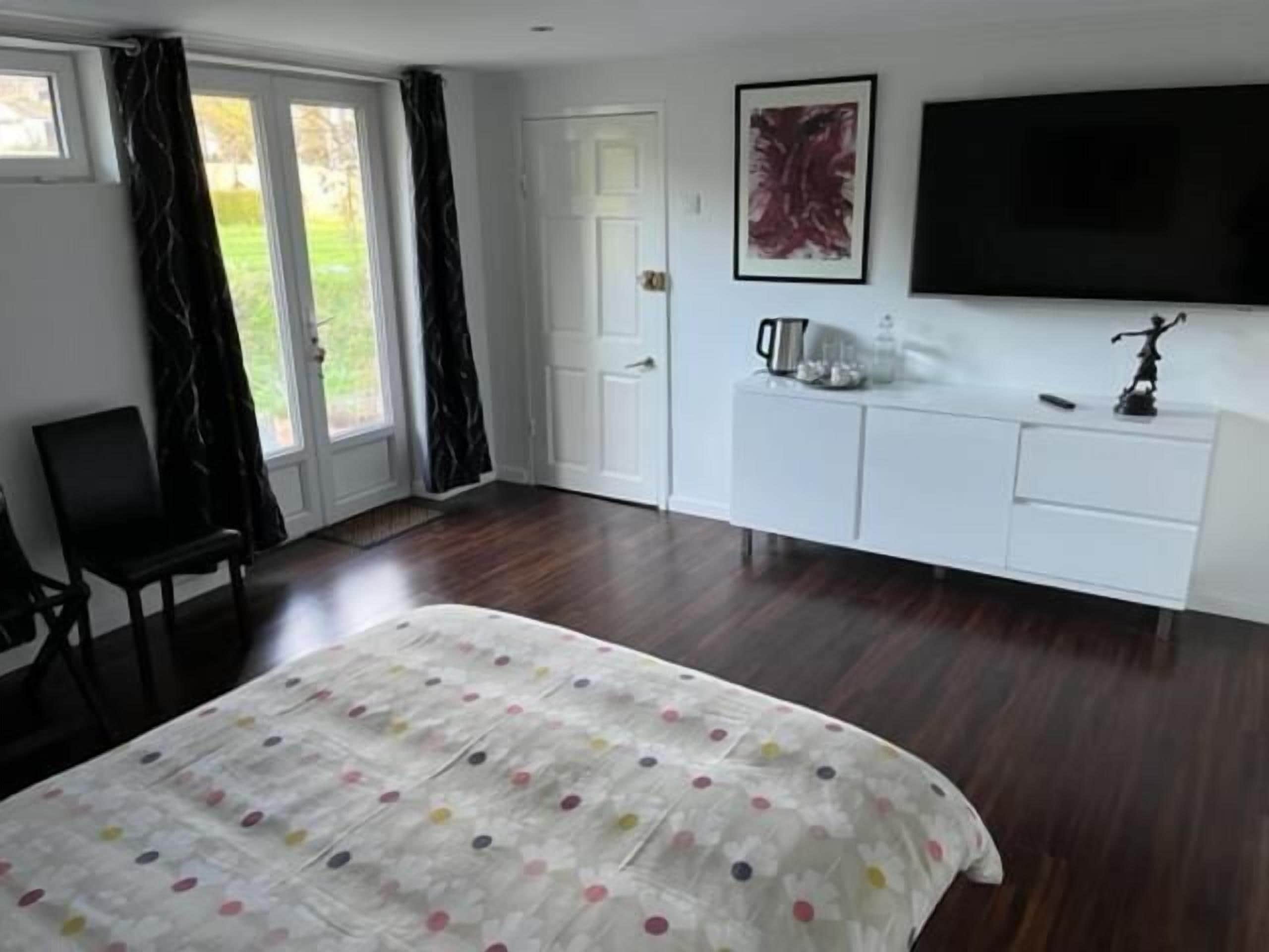 A bedroom with a bed, a TV, a white dresser, and a chair.