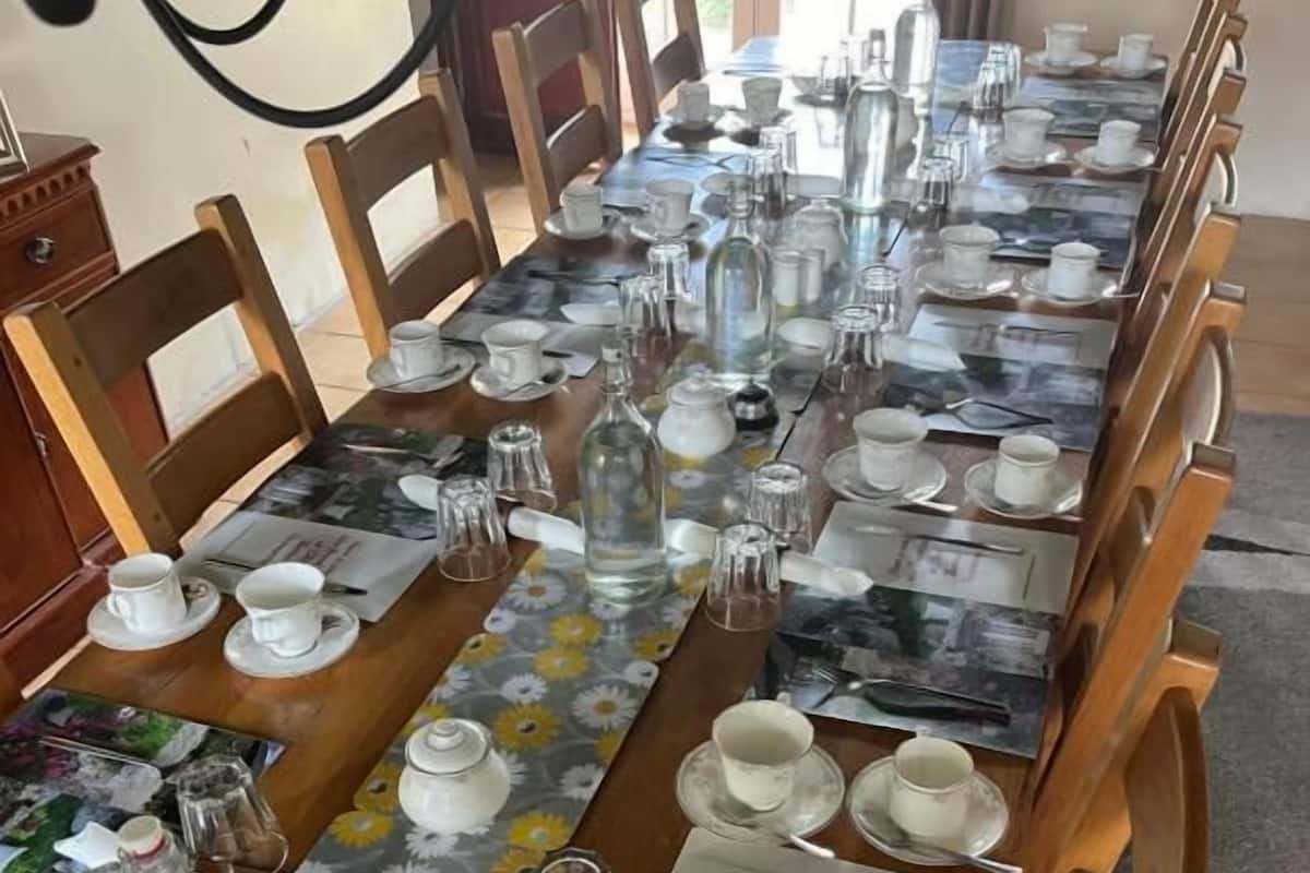 Una larga mesa de comedor dispuesta con múltiples sillas, copas de cristal y caminos de mesa con motivos florales.