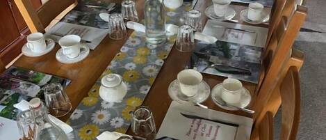 A long dining table set with multiple chairs, clear glassware, and floral table runners.