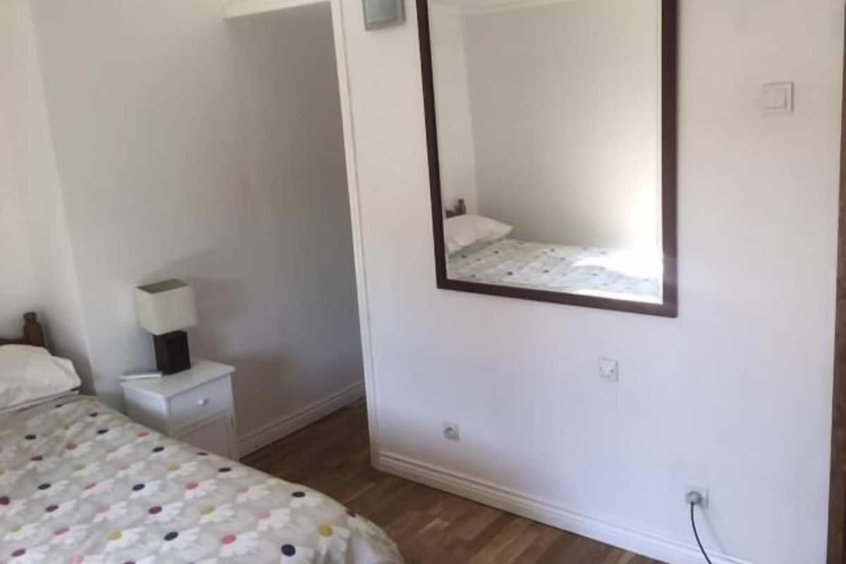 Un dormitorio con una cama, una mesita de noche, un espejo y un enchufe.