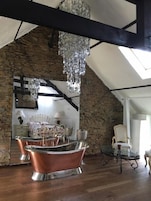 Una habitación con pared de piedra, un espejo grande, una cama, un candelabro y una bañera de cobre.