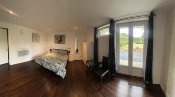 Un dormitorio con cama, una silla, un escritorio y un ventanal con cortinas.