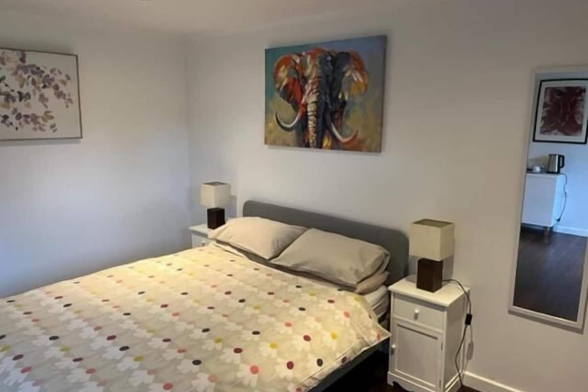 Un dormitorio con cama, mesitas de noche, un cuadro y vistas a una cocina.