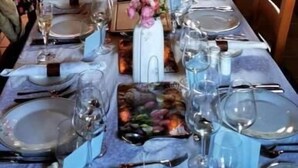 A long dining table set with candles, plates, and glasses, with a chandelier above.